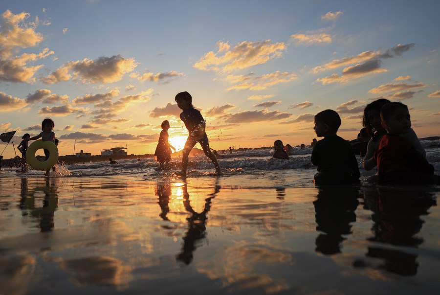 Palestinian children playing joyfully in ocean waves at sunset on Gaza's Mediterranean coastline